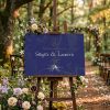 Panneau de bienvenue mariage Tolkien installé sur chevalet en bois à l’entrée d’une cérémonie en extérieur, décoration de mariage fantasy et forêt enchantée.